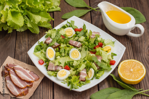 Salad with spinach, quail eggs and bacon. Wooden table. Top view. Close-up