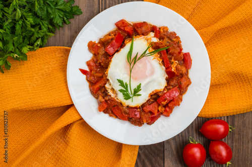 Shakshuka on a white plate. Traditional Jewish dish. Wooden table. Top view. Close-up