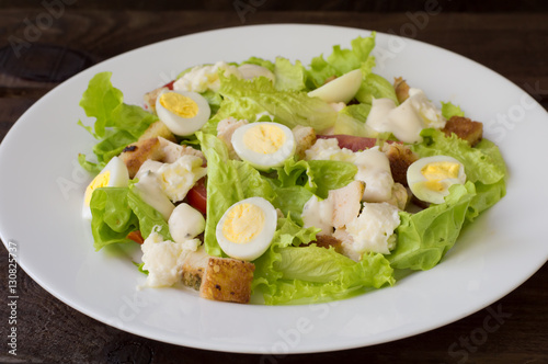 Salad with radishes, arugula, chicken and quail egg on a wooden background, top view
