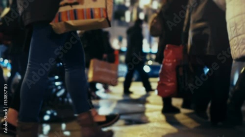 Christmas holiday shoppers at night, cross busy city street,slow motion 100p.Anonymous crowd of pedestrians cross a busy city street on a December night carrying shopping bags.No logos/faces visible