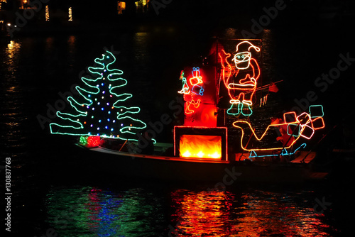 There goes the Merry Christmas float, bedecked in colorful lights, to share the joy of the holiday with Santa on his boat. photo