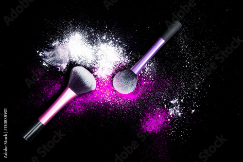 Make-up brushes with colorful powder on black background. Explosion stars dust with bright colors. White and purple and pink powder.