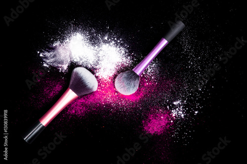 Make-up brushes with colorful powder on black background. Explosion stars dust with bright colors. White and pink powder.