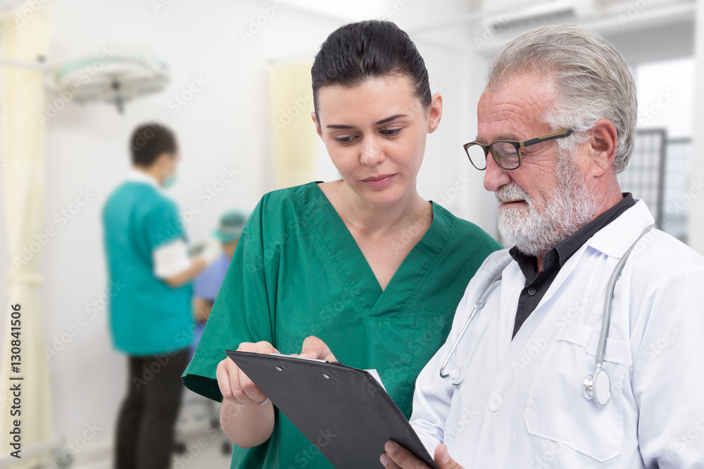 Senior doctor and nurse examine medical record in the hospital room Senior doctor and nurse examine medical record in the hospital room