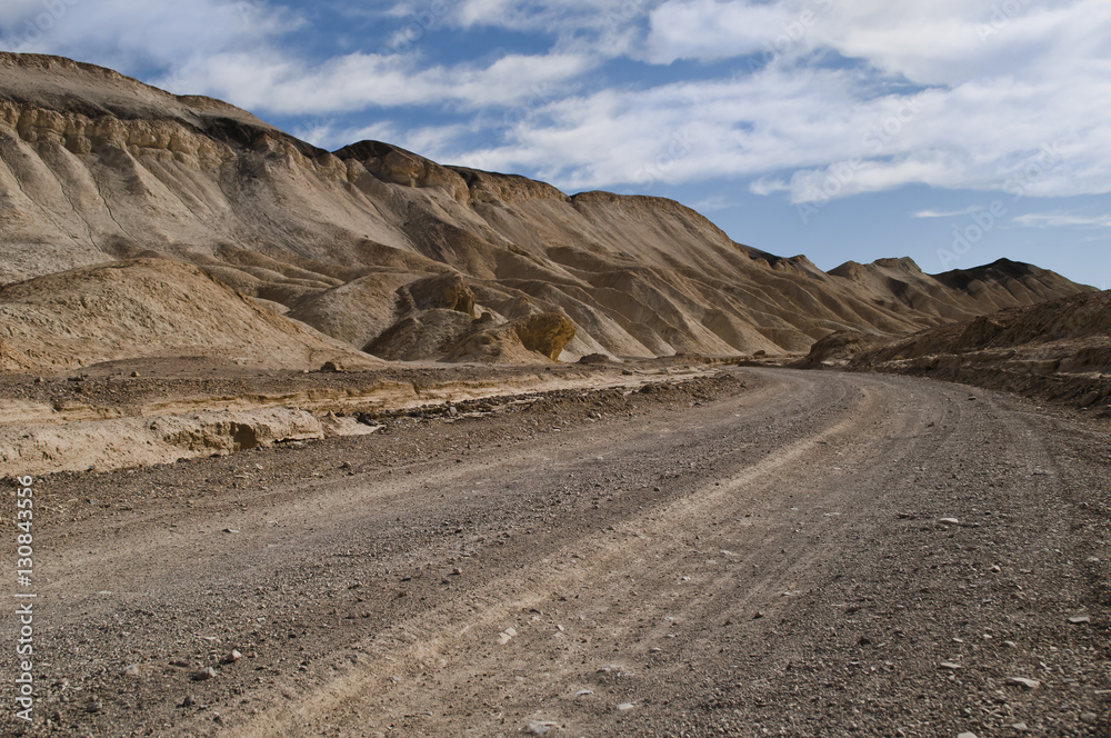 Dirt road through the Twenty Mules Canyon in the Death Valley National Park. Beautiful view of sandstone geological formation in a dry desert landscape, under a clear blue sky and midday light.