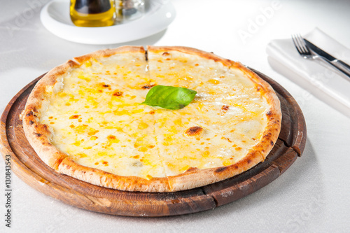 Four cheese pizza quattro fromaggi with basil leaf on a rustic wooden board on the served restaurant table photo