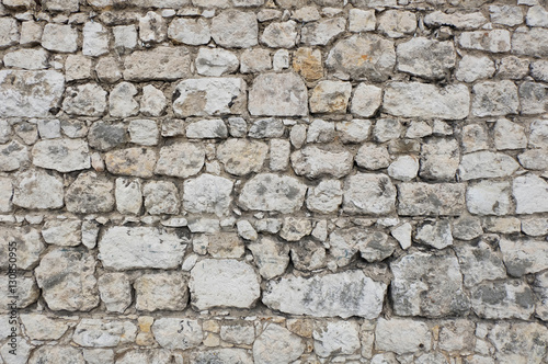 Antique stone wall of an ancient fortress   castle  mainly white and light colored stone blocks of varying sizes and shapes  creating an individual pattern   texture.