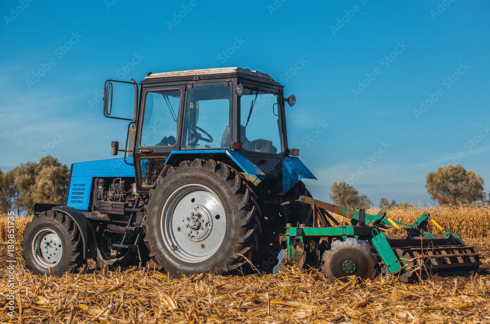 Autumn afternoon tractor rides and pulls the plow plow a field after harvest  of cereals - corn. On the ground are dry stalks. Stock Photo | Adobe Stock