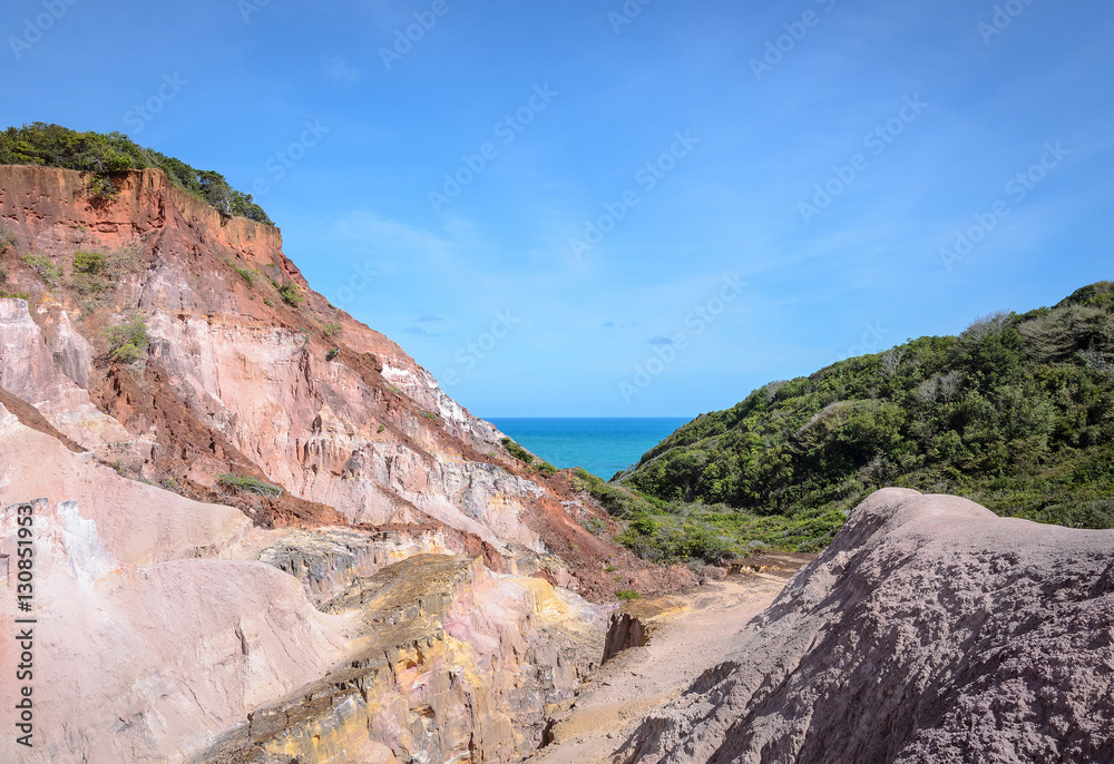 Obraz premium Canyon of cliffs with many stones sedimented by time, rocks with red and yellow colors and the sea in the background. Cliffs of Coqueirinho beach, PB - Brazil.