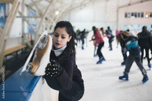 Pretty young woman stretching at ice-skating rink. 