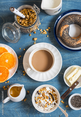 Yogurt, pumpkin granola, bagel, butter on a blue table. Breakfast set. Top view. Flat lay © okkijan2010