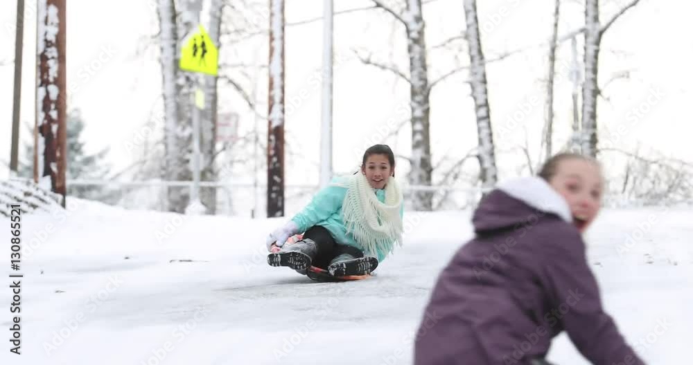 Two girls riding down an icy hill on snow sleds