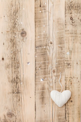 Knitted white heart Christmas decoration on retro wooden background with sparkling stars. Holiday season and celebration concept.