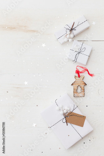 Top view on nice Christmas gifts wrapped in white gift paper, Christmas tree decorations on white wooden background with sparkling stars. New Year, holidays and celebration concept