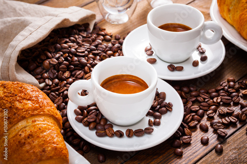 Two cup of espresso with a lot of coffee beans, with croissant, on wooden desk