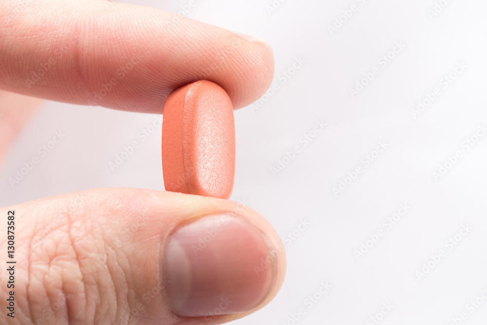 Fingers hold a red pill