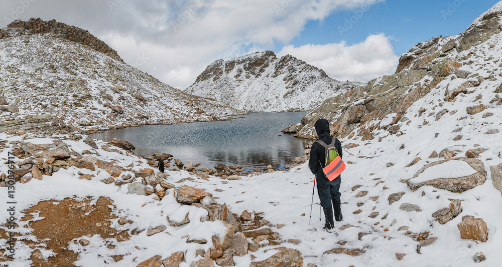 Hiker woman with backpack on snowy mountain peak at lake