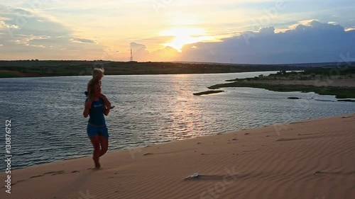 silhouette mother carries small girl on shoulders on sand dune against lake with sun reflection at sunset dusk photo