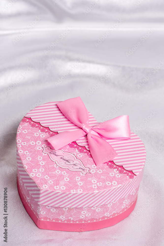 Pink heart shaped gift box with bow over white satin Pink heart shaped gift box with bow over white satin