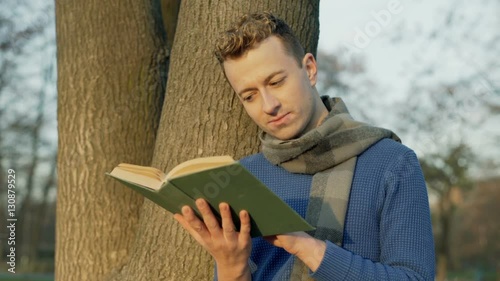 Man reading book next to the tree in the autumnal park, steadycam shot
 photo
