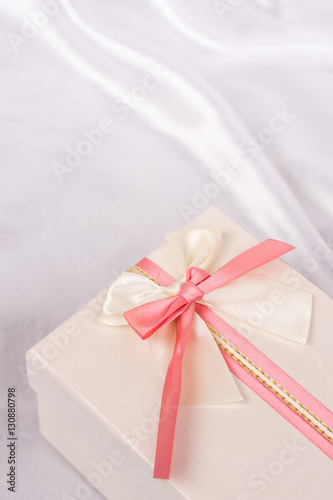 White gift box with red bow over white satin