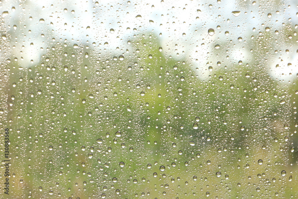 raindrops on the window with blurred green tree and sky background