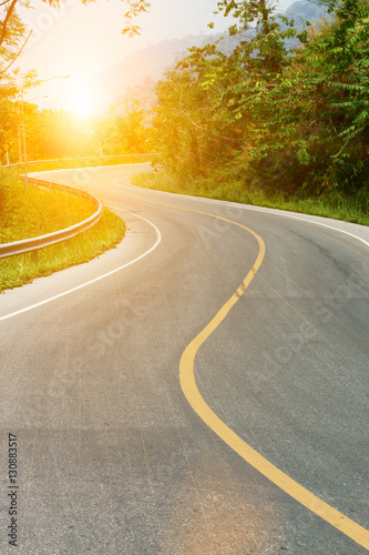 Asphalt road sharp curve along with tropical forest zigzag ahead with sun light.