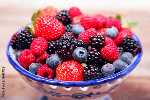Mixed ripe sweet berries in a blue and white bowl  with shallow depth of field. Blueberries raspberries  strawberries and blackberries. With space for text.