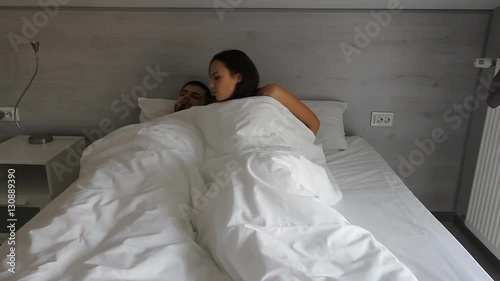 Cute happy young couple is waking up in the morning, kissing and cuddling up