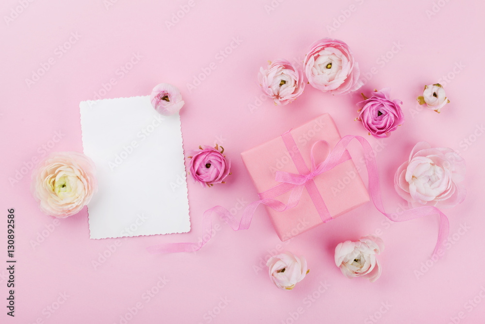 Gift or present box, white paper blank and beautiful spring flower on pink desk from above for wedding mockup or greeting card on womans day in flat lay style.