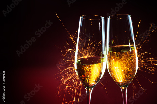 New Year party time with two champagne glasses and sparklers against a dark red background