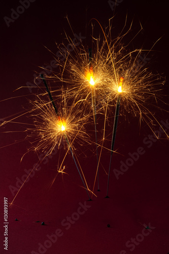 Three sparklers burning against a dark red background  party concept