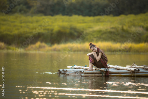 girl style alone, sitting on a bamboo raft in a river with lonel