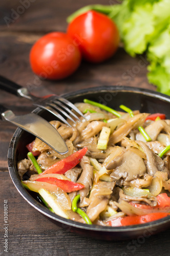 Stewed oyster mushrooms with vegetables in a pan. Wooden background. Top view. Close-up
