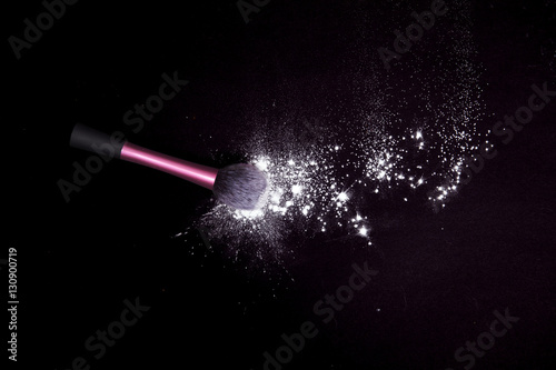 Make-up brush with colorful powder spilled glitter dust on black background. Makeup brush on new year's Party with bright colors. White powder on black table.