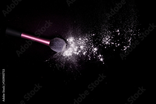 Make-up brush with colorful powder spilled glitter dust on black background. Makeup brush on new year's Party with bright colors. White powder on black table.