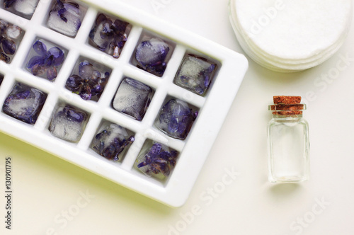 Ice cubs with frozen lilac flowers for cosmetic skincare use. Facial homemade tonic bottle, cotton pads. photo