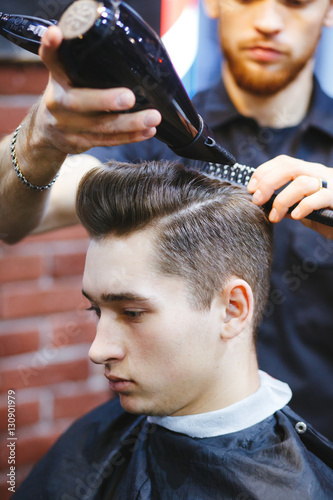 Male barber makes hair styling using a dryer.