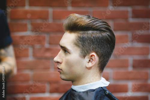 Male barber makes hair styling using a dryer.