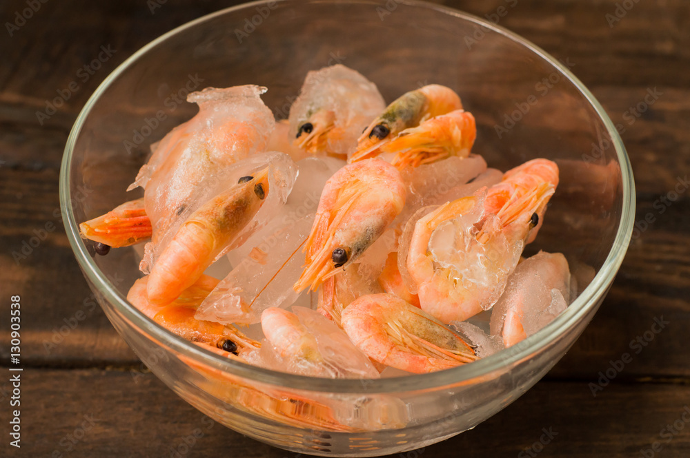 Frozen raw shrimp in a transparent plate of ice. Wooden background. Top view. Close-up Frozen raw shrimp in a transparent plate of ice. Wooden background. Top view. Close-up