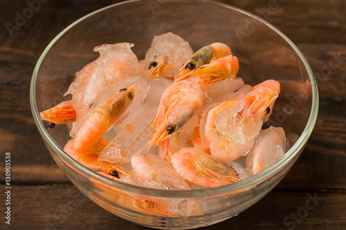 Frozen raw shrimp in a transparent plate of ice. Wooden background. Top view. Close-up