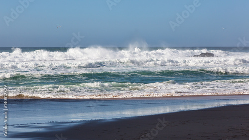Adraga Beach (Praia da Adraga) in Portugal. Beautiful place, golden sand. Rough sea, rocks, whitewash, blue sky.