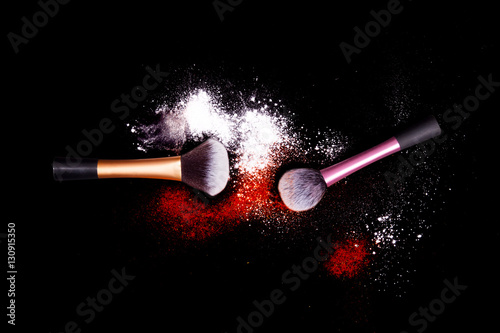 Make-up brushes with colorful powder spilled glitter dust on black background. Brushes with bright colors. White and red powder.