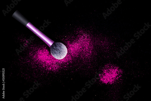 Make-up brush with colorful powder spilled glitter dust on black background. Makeup brush with bright colors. Pink powder on black table.