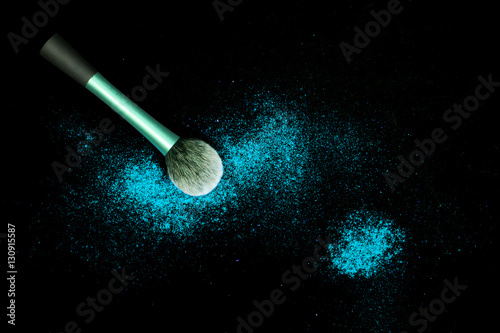 Make-up brush with colorful powder spilled glitter dust on black background. Makeup brush with bright colors. Turquoise powder on black table.