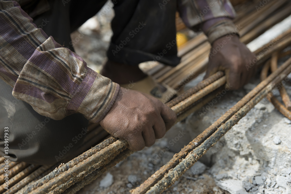 Closeup hands of the dirty worker in construction site.He is preparing steel bar for building house (construction)