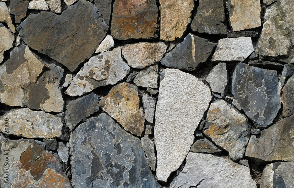 Stone wall consisting of various different colored stones in a mosaic like pattern. The shapes of the stone blocks are irregular but fitting precisely with only small gaps. Stone wall consisting of various different colored stones in a mosaic like pattern. The shapes of the stone blocks are irregular but fitting precisely with only small gaps.