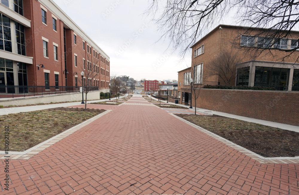 Deserted brick walkway with buildings and grassy areas  on either side. Horizontal.