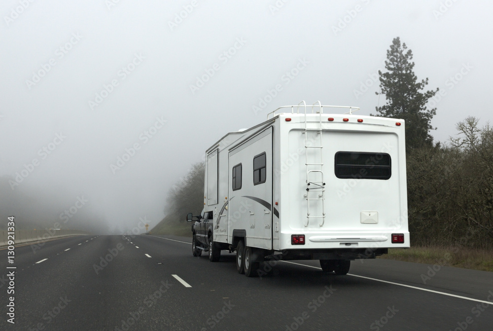 White RV camper driving into mountain fog. Horizontal.