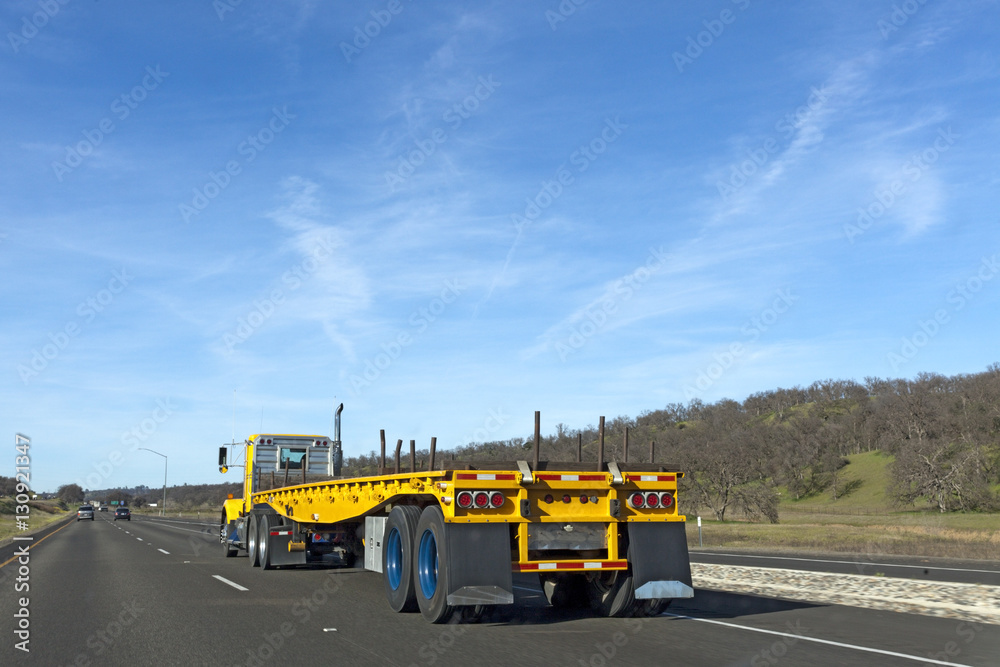 Obraz premium Yellow flatbed rig traveling on highway under blue sky. Copy space above.